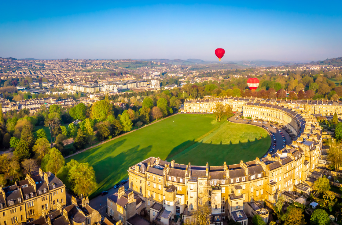Two air balloons hover over a green field surrounded by a half moon of buildings Two air balloons hover over a green field surrounded by a half moon of buildings