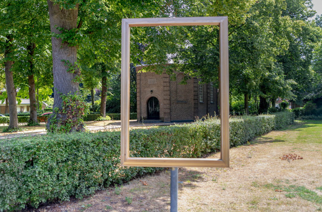 A metal frame in the middle of a garden, framing a building in the background.