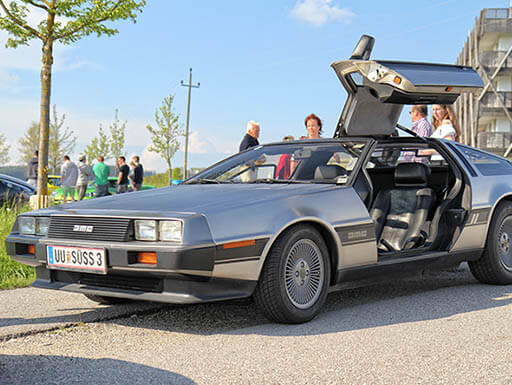 DeLorean car with side door open outside on the sunny day and people in the background