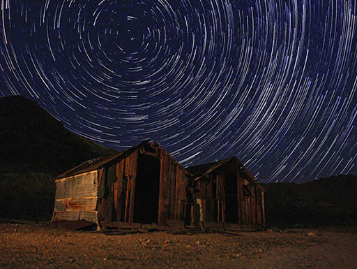 Night exposure of star trails light the night sky over two small wood sheds in California’s Death Valley.