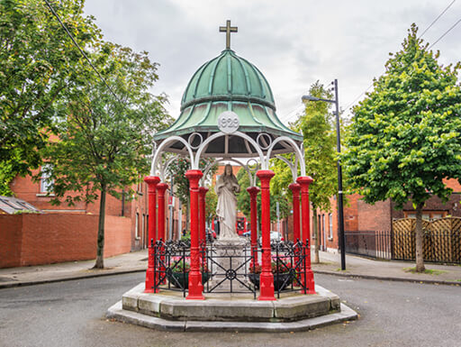 Statue of Jesus in the Liberties, Dublin, kept safe in a red gazebo structure surrounded by leafy green trees on a cloudy day in Ireland. Statue of Jesus in the Liberties, Dublin, kept safe in a red gazebo structure surrounded by leafy green trees on a cloudy day in Ireland.