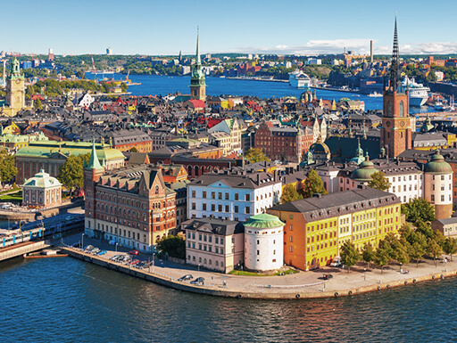 An aerial view of the Gamla Stan area in Stockholm, Sweden shows the colorful buildings right on the edge of the water on a clear, sunny summer day.