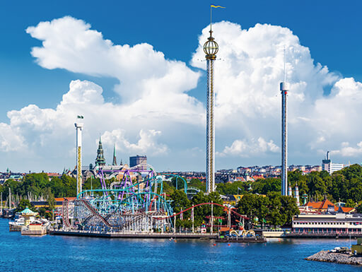 A view from across the water of the rollercoasters and rides of the theme park on Djurgarden, Stockholm, on a bright summer day. A view from across the water of the rollercoasters and rides of the theme park on Djurgarden, Stockholm, on a bright summer day.