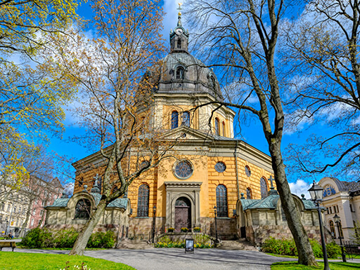 The exterior entrance of the Hedvig Eleonora Church in Ostermalm in Stockholm, Sweden with dark yellow stone surrounded by trees with new buds on a bright, early Spring day. The exterior entrance of the Hedvig Eleonora Church in Ostermalm in Stockholm, Sweden with dark yellow stone surrounded by trees with new buds on a bright, early Spring day.