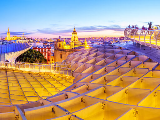 View from the top of the Space Metropol Parasol (Setas de Sevilla) in Seville, Spain shows the city illuminated in the evening as the last of the sun sets. View from the top of the Space Metropol Parasol (Setas de Sevilla) in Seville, Spain shows the city illuminated in the evening as the last of the sun sets.