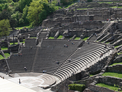 A daytime view from above of the ruins of the Roman theater in Lyon with grass growing over the stone and surrounding it in lush greenery. A daytime view from above of the ruins of the Roman theater in Lyon with grass growing over the stone and surrounding it in lush greenery.