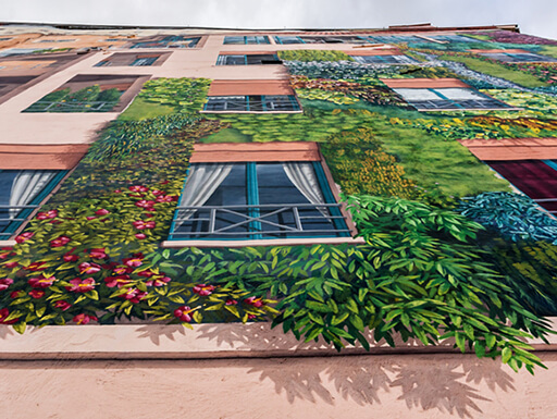 View from below of the realistic Mur des Canuts mural with windows surrounded by lush green plants on a cloudy afternoon in Lyon, France. View from below of the realistic Mur des Canuts mural with windows surrounded by lush green plants on a cloudy afternoon in Lyon, France.
