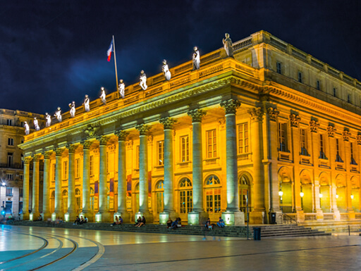 A nighttime view of the impressively columned Grand Theatre in Bordeaux, France illuminated against the dark sky. A nighttime view of the impressively columned Grand Theatre in Bordeaux, France illuminated against the dark sky.