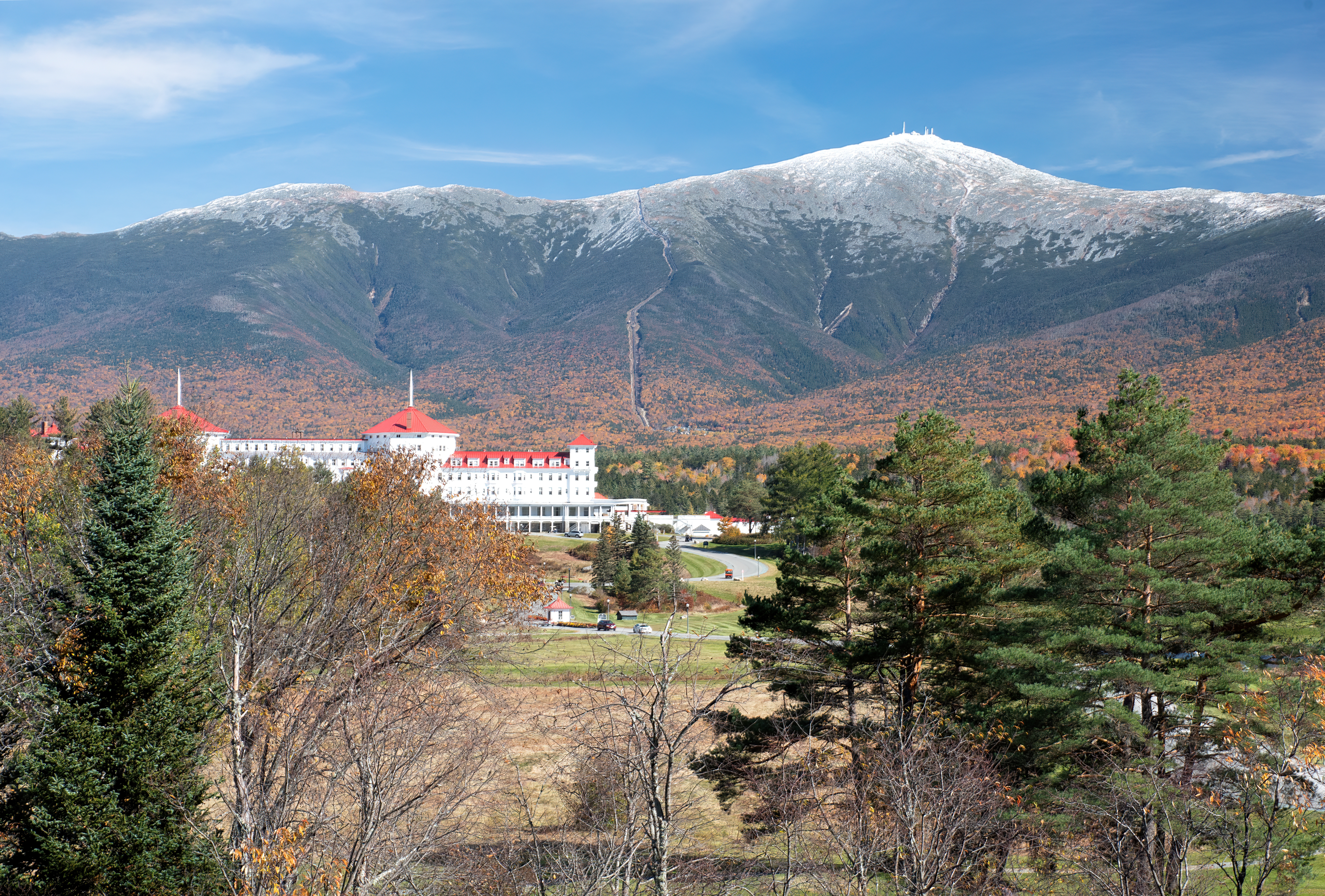 Colorful autumn scene at Bretton Woods, New Hampshire. Blue sky with dusting of snow on summit of Mount Washington, vibrant fall foliage, and red roof of historic Mount Washington Hotel. Mount Washington