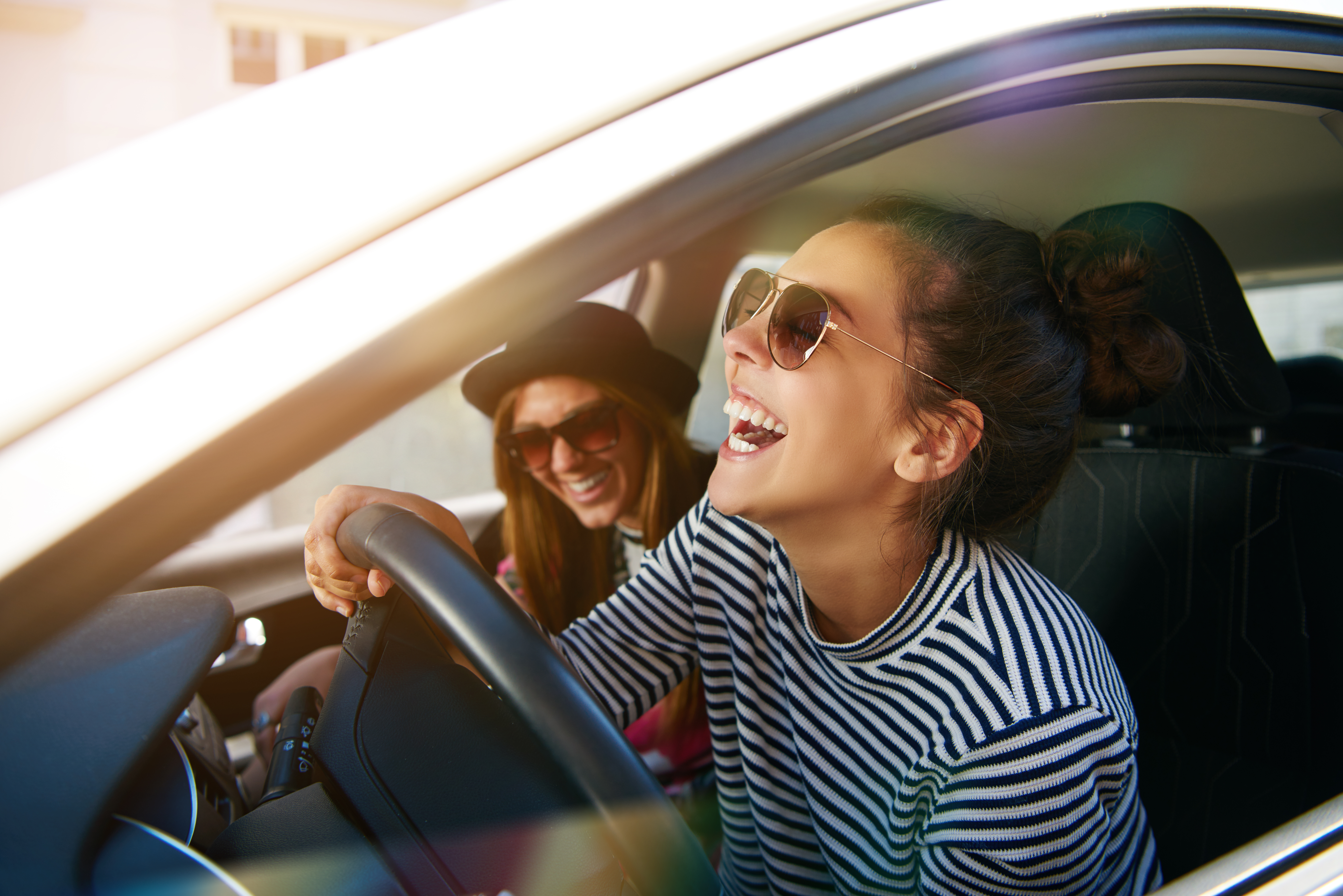 Laughing young woman wearing sunglasses driving a car with her girl friend , close up profile view through the open window; Shutterstock ID 529724287; purchase_order: ; job: 1287385; client: Hertz US; other: Cem Tezgoren